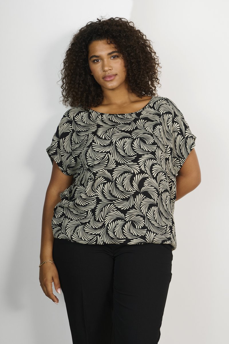 Haut noir avec un motif de feuilles beiges, coupe loose, col large et manches courtes. Associé à un pantalon noir. Texture lisse.