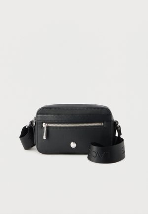 Black rectangular crossbody bag with front zip pocket, silver zipper, and adjustable strap with embossed brand name.