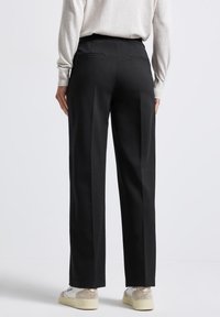 Pantalon noir à coupe droite, avec une texture lisse, deux poches arrière et une taille haute. Assorti à des baskets beiges.