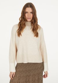 Hellbeige gestrickter Pullover mit hohem Kragen, gerippten Bündchen und Saum. Kombiniert mit einem braunen Rock im Leopardenmuster, der ein fließendes Design aufweist.