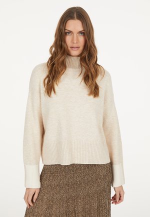 Hellbeige gestrickter Pullover mit hohem Kragen, gerippten Bündchen und Saum. Kombiniert mit einem braunen Rock im Leopardenmuster, der ein fließendes Design aufweist.