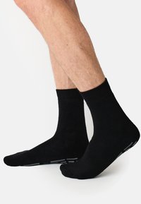 Sorte bomuldssokker med ribbet tekstur, midt på læggen, og grå accenter på sålerne. Glat finish og tætsiddende pasform omkring anklerne.