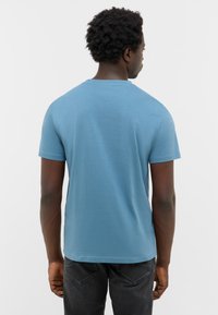 T-shirt à manches courtes, col rond, en coton bleu clair. Texture lisse avec une coupe décontractée, sans motifs ni accents visibles.
