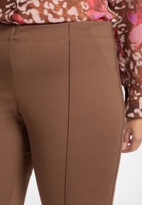 Brązowe dopasowane spodnie z elastycznego materiału, z pionowymi szwami, gładką fakturą i średnio podwyższonym stanem.