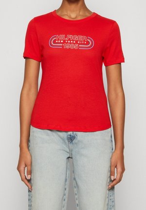 Rød bomulds t-shirt med korte ærmer og rund hals. Har et trykt design med teksten "HILFIGER NEW YORK CITY 1985" i blå og hvid på fronten.