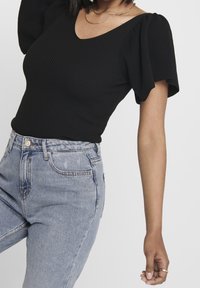 Top corto de manga corta negro acanalado con escote en V, que presenta sutiles mangas abullonadas. Combinado con jeans de tiro alto de color azul claro.