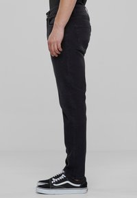 Jeans de denim negro de corte slim, hechos de algodón, con cinco bolsillos y un acabado limpio. Combinados con zapatillas negras y blancas.