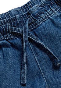 Tela de mezclilla azul oscuro con una cinturilla elástica y cordones. Detalles notables incluyen textura y costuras visibles.