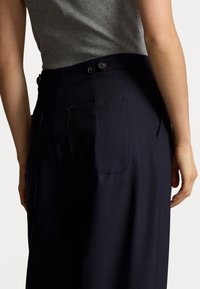 Marina skräddarsydda byxor med två bakfickor, tygtextur synlig. Har två mörka knappar i midjan och en rak bendesign.