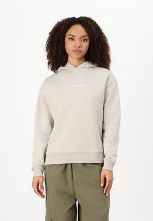 Grå hettegenser med snorhette og ribbede mansjetter, med "Calvin Klein" logo i hvitt. Kombinert med olivengrønne cargo-bukser.