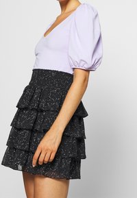 Top corto de color lila con cuello en V, combinado con una falda negra de volantes con un patrón moteado y cintura elástica.