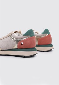 Sneaker con una tomaia in suede beige, dettagli in metallo dorato, dettagli sul tallone in suede rosa e verde, e una suola in gomma nera.