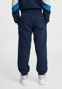 Marinblå joggers gjorda av mjukt material, med elastisk midja och ärmslut. Distinkta sidostråk och en avslappnad passform kompletterar designen.