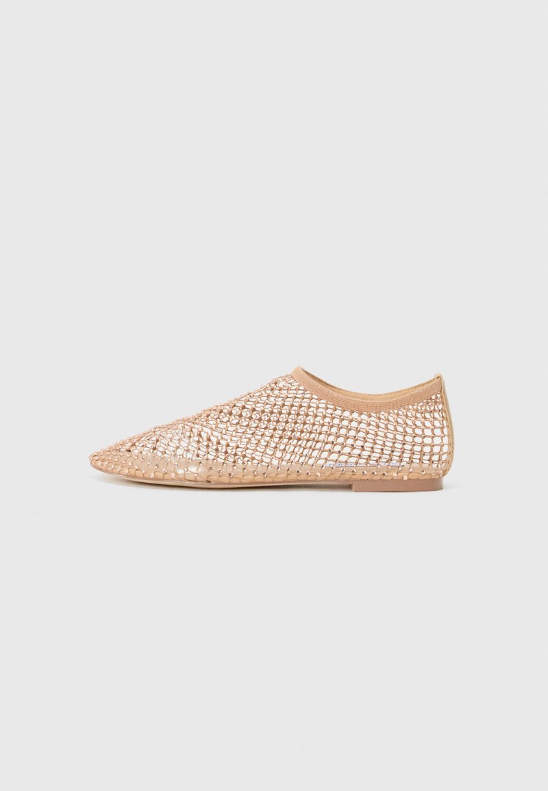 Chaussure plate beige avec un bout pointu et un design en maille tissée ouverte, bord élastique à la cheville et semelle fine sur un fond uni.