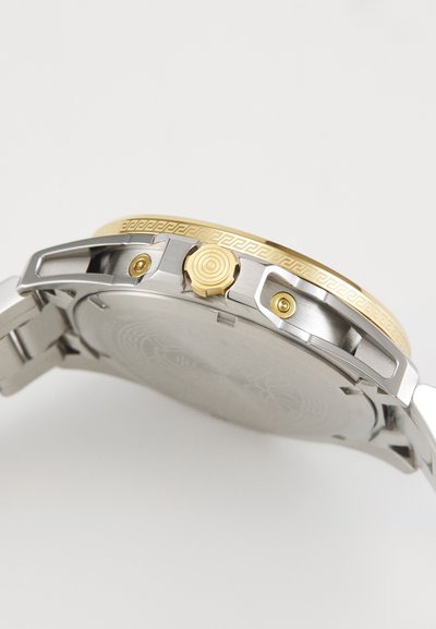 Orologio in acciaio inossidabile con lunetta dorata. Caratterizzato da una corona testurizzata e un fondello inciso in dettaglio. Schema di colori argentato e dorato.