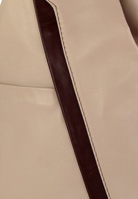 Beige Ledertasche mit einem dunkelbraunen Lederriemen, kontrastierender Naht, glatter Textur und minimalistischem Design.