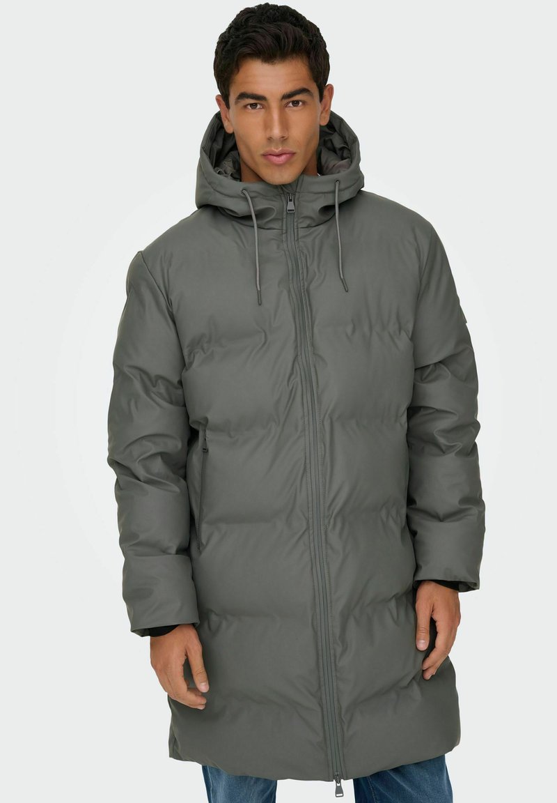 Manteau matelassé gris avec capuche, avec un design mi-long, des cordons élastiques et une fermeture éclair à l'avant. Tissu texturé pour la chaleur.