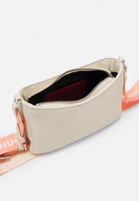 Beige leather crossbody bag with a zip closure, orange adjustable strap, and interior pocket featuring a red cardholder.