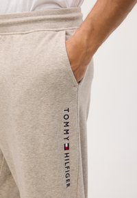 Pantaloni de trening gri deschis, dintr-un amestec de bumbac, cu buzunare laterale și logo-ul brodat "TOMMY HILFIGER" pe piciorul stâng.