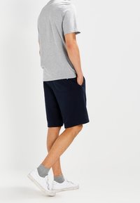 Camiseta de algodón gris, pantalones cortos de sudadera azul marino con bolsillos laterales, y zapatillas blancas con calcetines grises, vistas desde la parte de atrás.