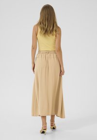 Lysegul ribbet tanktop parret med en lang, svævende beige nederdel med elastisk talje. Modellen bærer gule hæle sandaler.