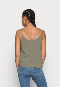 Débardeur vert olive avec des fines bretelles croisées et une texture lisse, associé à un jean bleu avec un design de poche classique.