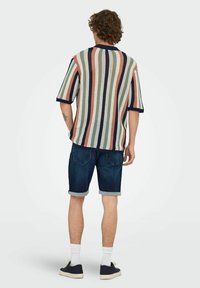Top de punto de manga corta con rayas multicolores en verde, coral y azul marino. Combinado con pantalones cortos de mezclilla oscura y calcetines blancos.