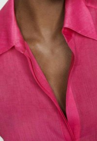 Chemise en lin rose avec col, fermeture à boutons et une texture douce et légère. Coutures visibles le long des bords.