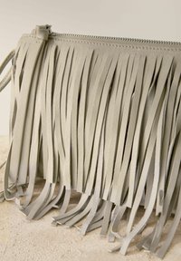 Torebka crossbody z frędzlami w jasnoszarej skórze. Posiada długie, teksturowane frędzle oraz zamek błyskawiczny u góry. Kompaktowy i wszechstronny design.