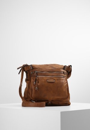 Brun læder crossbody taske med flere lynlåslommer og justerbar rem, placeret på en hvid piedestal mod en ensfarvet baggrund.