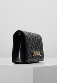 Borsa trapuntata in ecopelle nera con dettagli in metallo dorato e design strutturato, dotata di un unico scomparto e base piatta.