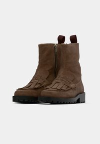 Bottines en daim marron à fermeture éclair frontale, avec des détails tissés sur le bout et une semelle noire texturée. Elles sont dotées de languettes pour un enfilage facile.