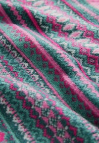 Textile avec des motifs géométriques verts, roses et blancs en bandes répétitives sur une surface de tissu tissé texturé.