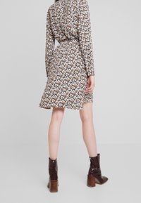 Långärmad blommig klänning med mönster i brunt, krämvitt och orange. Hög midja, utsvängd nederkant och tillsammans med knähöga bruna klackstövlar.