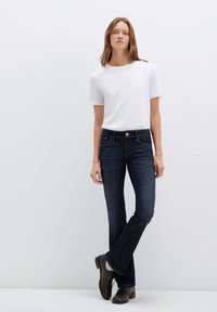 Jeans in denim blu scuro con vestibilità a gamba dritta, abbinati a una t-shirt bianca a maniche corte e scarpe eleganti nere. Design semplice, senza decorazioni.