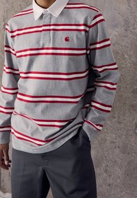 Langarm-Poloshirt aus grauer Baumwolle mit rot-weißen horizontalen Streifen, ausgestattet mit einem klassischen Kragen und einem kleinen Logo auf der Brust.