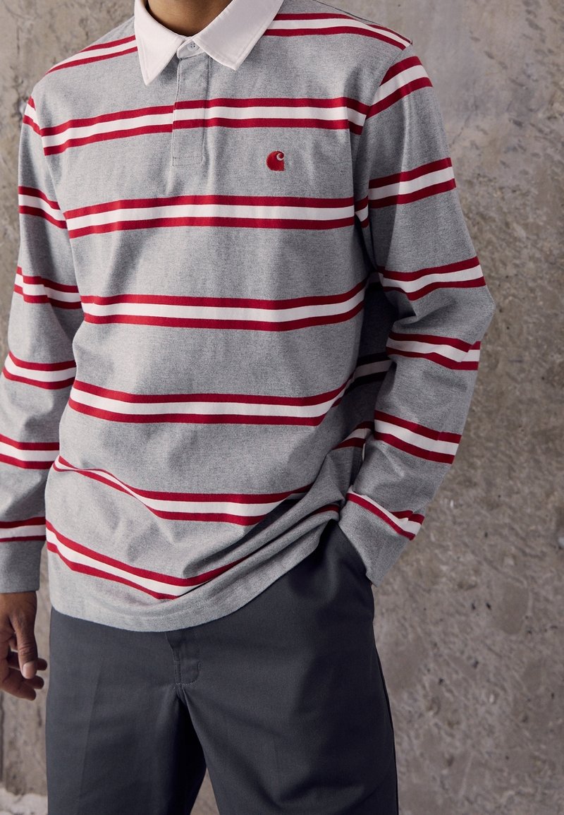 Langarm-Poloshirt aus grauer Baumwolle mit rot-weißen horizontalen Streifen, ausgestattet mit einem klassischen Kragen und einem kleinen Logo auf der Brust.