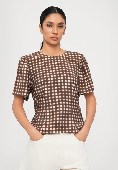 Camisa de manga corta a cuadros marrones y blancos con cuello redondo. Textura suave y silueta ajustada, combinada con pantalones de color claro.