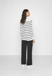 Ribbet, hvit og svart stripete genser med lange ermer og høy hals, parret med svarte vide bukser og hvite joggesko.