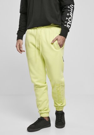Pantaloni de trening galbeni neon cu manșete elastice, talie cu șnur și buzunare laterale. Prezintă logo-ul "SOUTHPOLE" imprimat vertical. O pereche de adidași negri.