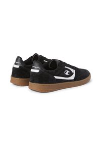 Schwarze Wildleder-Sneaker mit einem weißen Logo, entworfen in einem niedrigen Profil, mit Gummiaußensohle und kontrastierender Gummisohle für besseren Halt.