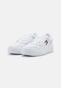 Sneaker basse bianche con finitura in pelle liscia, dettagli perforati e una patch con logo in rosso, bianco e blu sul lato.