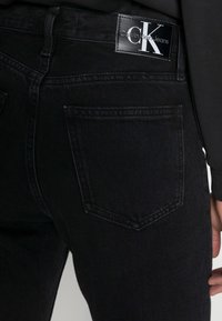 Černé denimové džíny mají úzký střih, standardní kapsy a štítek značky Calvin Klein na zadním pásu.