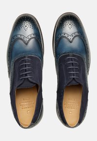 Scarpe di pelle in pelle scura con una finitura a gradiente liscia. Presentano un design wingtip, dettagli brogue e accenti in camoscio. Chiusura con lacci.