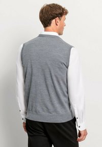 Grijze gebreide vest met ronde hals, met een gladde textuur en geribde zoom, gedragen over een witte blouse met lange mouwen.