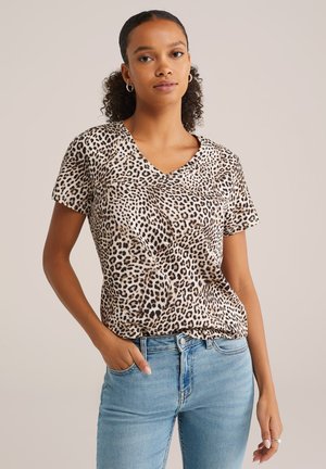 Bež in rjav t-shirt s kratkimi rokavi in V-izrezom v leopardjem vzorcu, narejen iz lahkega materiala, v kombinaciji z svetlo modrimi jeans hlačami.