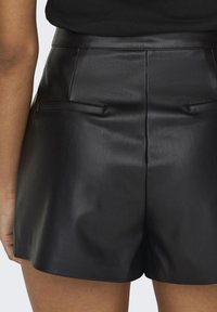 Zwarte leren shorts met een gladde textuur, voorzien van twee kleine zakken en een aansluitende taille. Het ontwerp is minimalistisch en op maat gemaakt.