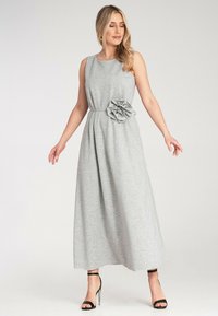 Szara, bezrękawnikowa sukienka maxi z dopasowaną talią i kwiatowym akcentem z boku; wykonana z miękkiego materiału o gładkiej fakturze.