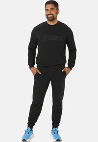 Ensemble de sweat-shirt noir et de joggers avec le logo "asics" en relief, fabriqué en tissu lisse. Les pantalons sont dotés de poches latérales et de poignets côtelés ; baskets bleues.