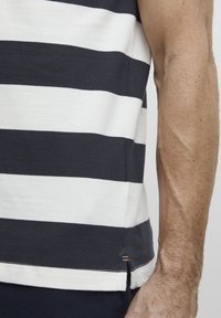 Camiseta a rayas en algodón azul marino y blanco, con cuello redondo y aberturas laterales en el dobladillo con detalles de costura.